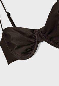Gros plan d'une coque de soutien-gorge noir à armatures avec bretelles fines ajustables sur un fond clair uni.