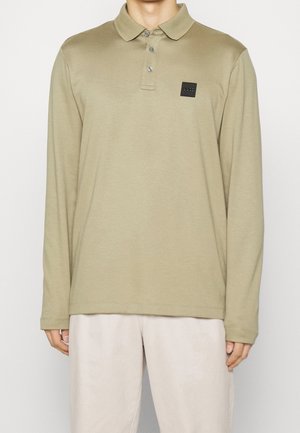 Polo à manches longues en vert olive doux, fabriqué en tissu doux, avec un col, trois boutons et un petit écusson logo noir.