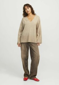 Beige stickad v-ringad tröja med ribbad fåll, kombinerad med lösa bruna jeans och röda ballerinas. Tyget har ett mjukt, strukturerat utseende.