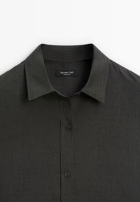 Camicia button-up in tessuto verde scuro con una finitura testurizzata. Presenta un colletto classico e tre bottoni marroni lungo la parte anteriore.