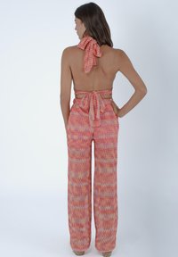 Vista posteriore di un top a halter e pantaloni a gamba larga con un motivo chevron multicolore, caratterizzati da una fascia legata al collo e in vita, nei toni dell'arancione e del rosa.