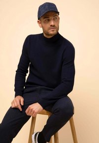 Námořnický modrý žebrovaný rolák s odpovídajícími kalhotami, doplněný džínovou čepicí. Tento outfit se vyznačuje texturovanou látkou a přiléhavým střihem.