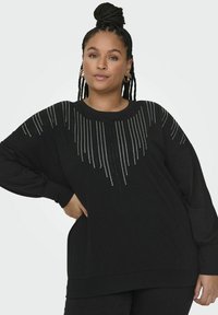 Černá mikina s volným střihem, dlouhými rukávy a dekorativním vzorem z stříbrných cvočků uspořádaných do gradientu, což vytváří texturovaný vzhled.