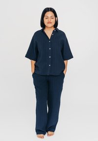 Marineblauwe, kortekorte mouw knoopshirt met verticale strepen, gecombineerd met bijpassende wijde broek. Zachte stof, relaxte pasvorm, zijzakken.