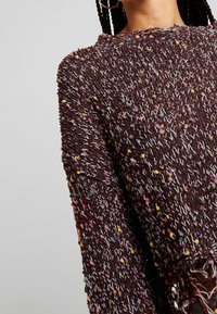 Brauner Strickpullover mit bunten Sprenkeln, Rundhalsausschnitt und langen Ärmeln. Der Pullover hat eine lockere Passform und einen strukturierten Stoff.