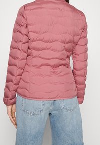 Světlounce růžová prošívaná péřová bunda s výraznými vodorovnými švy, střihově přiléhavá s stojatým límcem, kombinována s džínami s vysokým pasem.