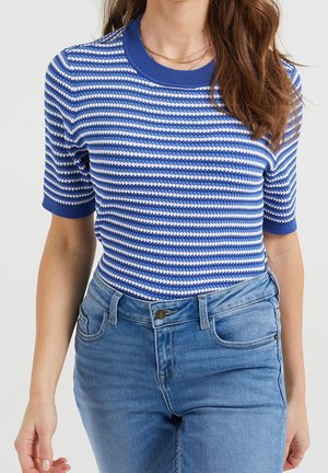 Kvinde iført blå- og hvidstribet kortærmet sweater stoppet ned i højtaljede blå jeans med knap- og lynlåslukning.