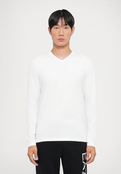 Witte v-hals t-shirt met lange mouwen, gemaakt van zachte stof, met een aansluitend ontwerp. Draag het met zwarte broeken met een grafische print.