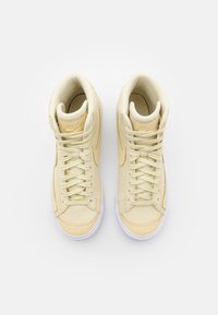 High-top sneakers i ljusbeige läder med matchande snören, vit gummisula och subtil branding på tungan. Texturerade sidopaneler.