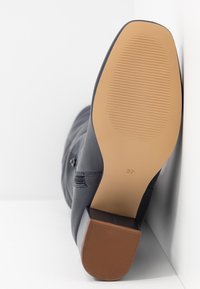 Botte en cuir noir avec un bout rond, petit talon et semelle en caoutchouc. Présente une finition lisse et une fermeture éclair latérale. Taille 37 indiquée sur la semelle.