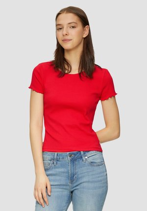 Czerwony obcisły t-shirt z krótkim rękawem i okrągłym dekoltem, z falbaniastymi krawędziami, w zestawie z jasnoniebieskimi dżinsami. Brak widocznych logo lub wzorów.