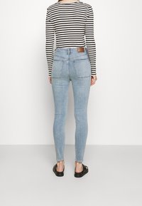 Světle modré skinny džíny s vysokým pasem a hladkou texturou, s dvěma zadními kapsami a hnědou koženou etiketou na pase.