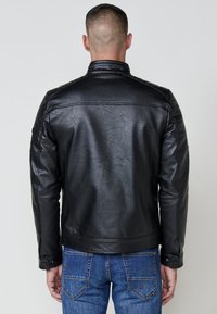 Giacca in pelle nera con una texture liscia, vestibilità slim e colletto rialzato. Presenta dettagli con spalle trapuntate e polsini con bottoni.