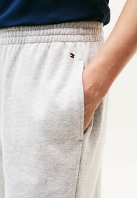 Lichtgrijze sweatpants met een elastische tailleband en zijzakken. Een klein logo met rode en blauwe accenten is zichtbaar nabij de zak.