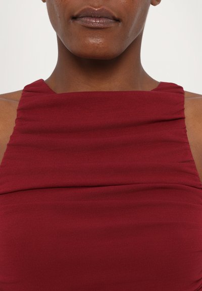 Burgunderfarbene ärmellose Bluse mit gerafftem Material am Ausschnitt, aus einem weichen, elastischen Stoff gefertigt, der ein tailliertes Design betont.