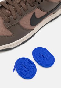 Nike tenisky s hnedým syntetickým vrchom a čiernymi akcentmi, doplnené dvoma modrými okrúhlymi šnúrkami na bielom pozadí.