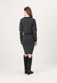 Robe en tricot avec un motif géométrique noir et gris, à manches longues, avec des poignets côtelés et une silhouette ajustée, associée à des bottes noires jusqu'aux genoux.