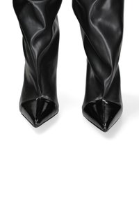 Bottes pointues noires à talons hauts en faux cuir lisse, avec un design supérieur drapé et des accents de pointe brillants.