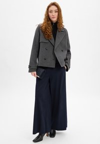 Grijze dubbelgeknoopte peacoat van wolmix, zwarte coltrui, wijde marineblauwe broek, zwarte laarzen met hak en een marineblauwe clutch. Soepele structuur.