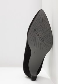 Chaussure à talon haut en suede noir avec une pointe effilée et une semelle en caoutchouc noir texturé avec branding, taille 37, sur fond blanc.