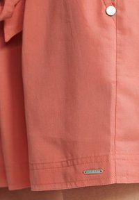 Coral cotton dress with a slightly structured design, featuring silver hardware and a stitched hem. A branded detail is visible at the bottom.