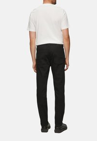 Jeans de mezclilla negra con corte slim, cinco bolsillos y un discreto detalle de canesú en la parte posterior. Combinados con una camiseta blanca sencilla.