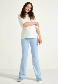 Lightweight cream short-sleeve sweater paired with pale blue flared pants and teal sneakers. Smooth texture with a relaxed fit throughout.