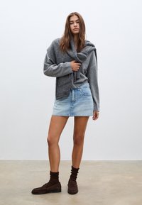 Grå oversized tröja, ljusblå denim minikjol, bruna mockaskor och bruna strukturerade strumpor. Enkelt mönster med en avslappnad look.