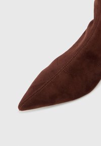 Bottine en suède marron à bout pointu, présentant une texture lisse, des détails de couture le long des coutures et une forme raffinée et effilée.