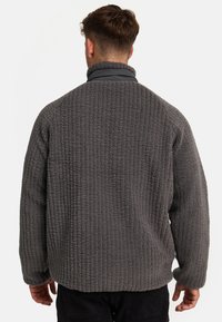 Grå fleecepullover med et tekstureret, ribbet mønster, der har en ståkrave og løs pasform. Stoffet ser blødt og varmt ud.