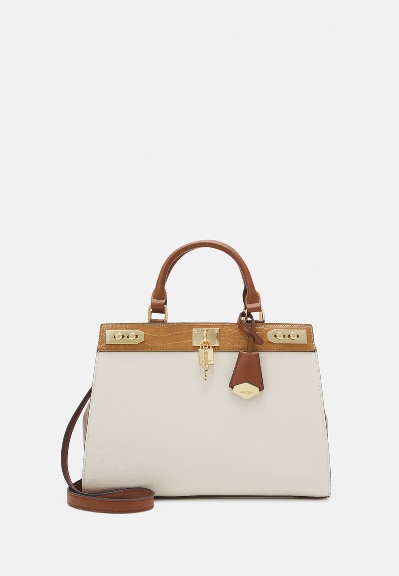 Sac à main blanc avec une bordure et des poignées en cuir camel. Il présente des accessoires dorés et un porte-clés en forme de clé. Comprend une bandoulière marron amovible.