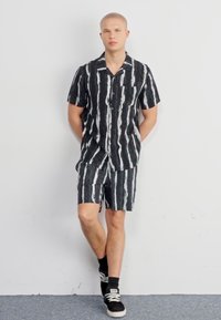 Camisa de rayas en blanco y negro de manga corta con pantalones cortos a juego, que presenta un corte relajado, bolsillo y un tejido ligero.