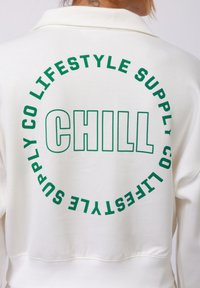 Valkoinen huppari, jossa on vihreä teksti. Takana on pyöreä kuvio, jossa korostuu "CHILL" ja sen ympärillä on teksti "CO LIFESTYLE SUPPLY". Pehmeä kangas, rento istuvuus.