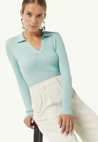 Helles blaues, geripptes Strickoberteil mit V-Ausschnitt und Kragen, kombiniert mit cremefarbenen, hoch geschnittenen Hosen mit vorderen Falten und seitlichen Taschen.