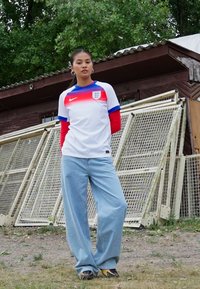 Balts Nike krekls ar sarkaniem un zilajiem akcentiem, kurā ir Anglijas emblēma. Saskaņots ar gaiši ziliem platām kājām džinsiem un melniem sporta apaviem.