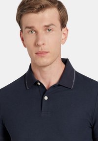 Granatowa koszulka polo z kołnierzykiem, trzema guzikami z przodu i białymi zdobieniami. Wykonana z bawełny, z delikatnym logo na piersi.