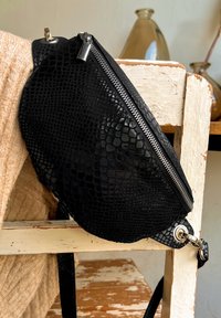 Sort faux læder taske med et struktureret reptil mønster, sølv lynlås og hardware accenter, der har et buet design og justerbar rem.