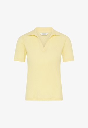Gaiši dzeltena īsroku polo kreklā ar atvērtu V-veida apkakli, izgatavota no mīkstas adītas auduma, attēlota uz baltas fona.