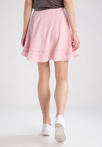 Falda pink de campana hecha de tejido ligero, con costuras decorativas y un acabado suave, combinada con zapatos blancos.