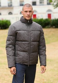 Harmaa toppatakki korkealla kauluksella, vetoketjukiinnityksellä, tikattu design ja teksturoitu kangas. Yhdistetty tummiin housuihin, sumeaa ulkoista taustaa vasten.