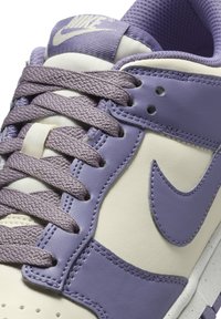 Purple and cream sneaker with textured leather, matching laces, and a rubber sole. Features a signature logo on the side and stitched details.