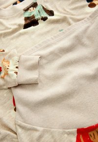 Kerge beež sviiter, millel on karu ja pühade teemalised mustrid, soonikkoes mansetid ning tekstureeritud kangas pehme ja siledaga viimistlusega.