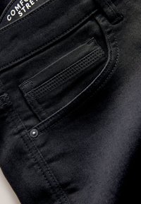 Primer plano del bolsillo de unos vaqueros vaqueros negros con costuras detalladas y un pequeño remache de metal cerca de la costura.