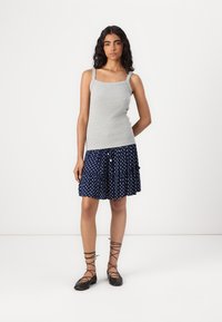 Top grigio senza maniche con spalline sottili, abbinato a una gonna blu navy a pois con balze. Ballerine nere stringate completano l'outfit.