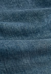 Denim tkanina tamnoplavih boja s vidljivom teksturom tkanja, prikazujući blage varijacije u boji i mekan završetak.