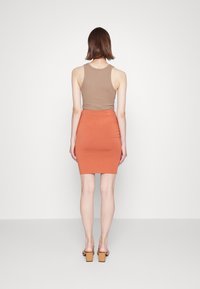 Hnědý bezrukávový top v kombinaci s těsným oranžovým sukněm, hladký materiál, délka nad kolena a sandály na blokovém podpatku.