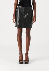 Schwarzer Leder-Minirock mit vorderen Taschen, der eine glatte Textur und einen geraden Schnitt aufweist. Tragen mit schwarzen High Heels mit Knöchelriemen.