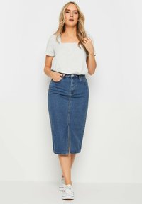 Granatowa spódnica dżinsowa z rozporkiem z przodu, zestawiona z jasnoszarym topem z krótkim rękawem. Całość uzupełniają białe trampki.