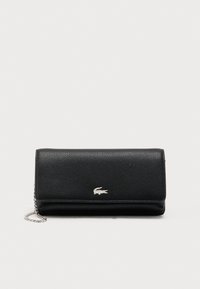 Bolso de mano de cuero negro texturizado con correa de cadena plateada y pequeño logo de cocodrilo plateado en la solapa frontal.