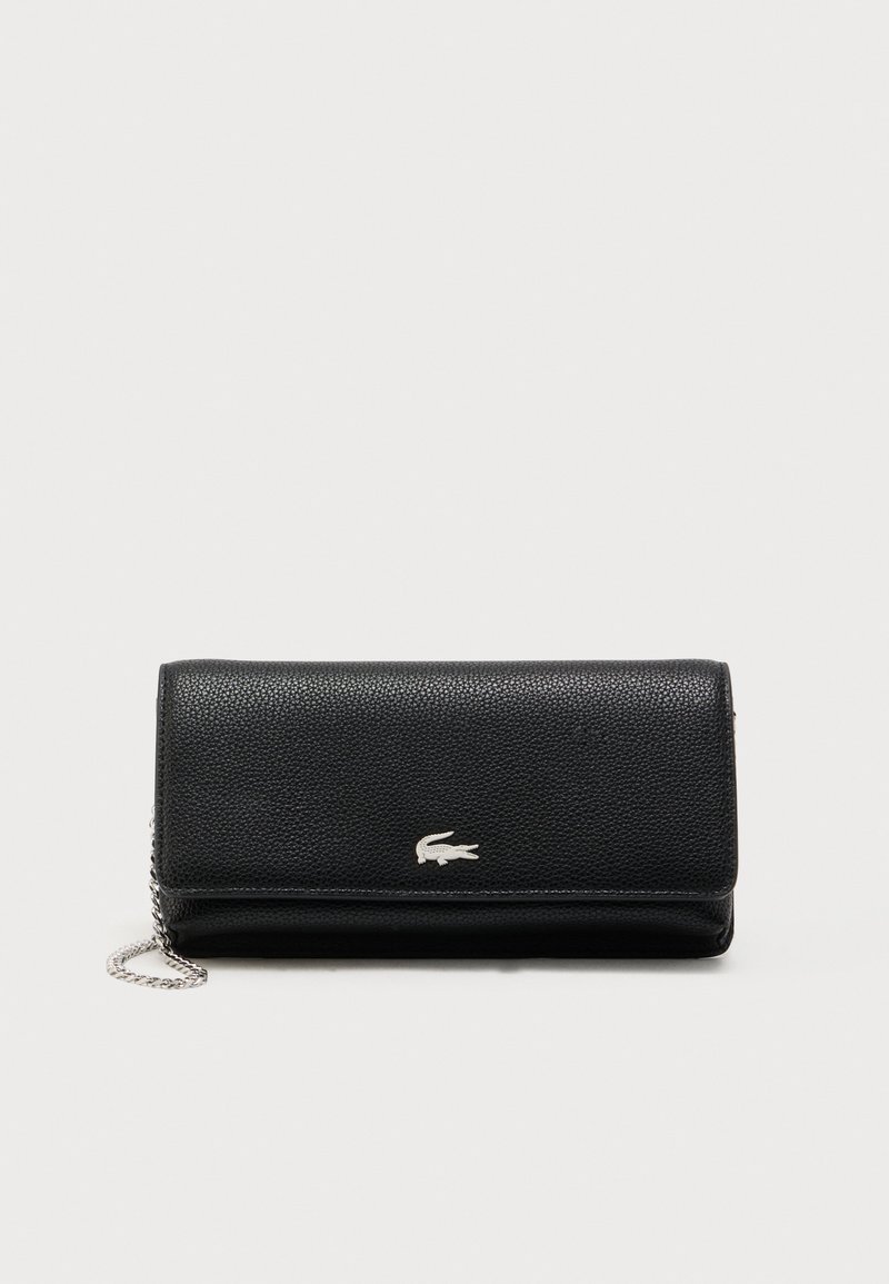 Bolso de mano de cuero negro texturizado con correa de cadena plateada y pequeño logo de cocodrilo plateado en la solapa frontal.